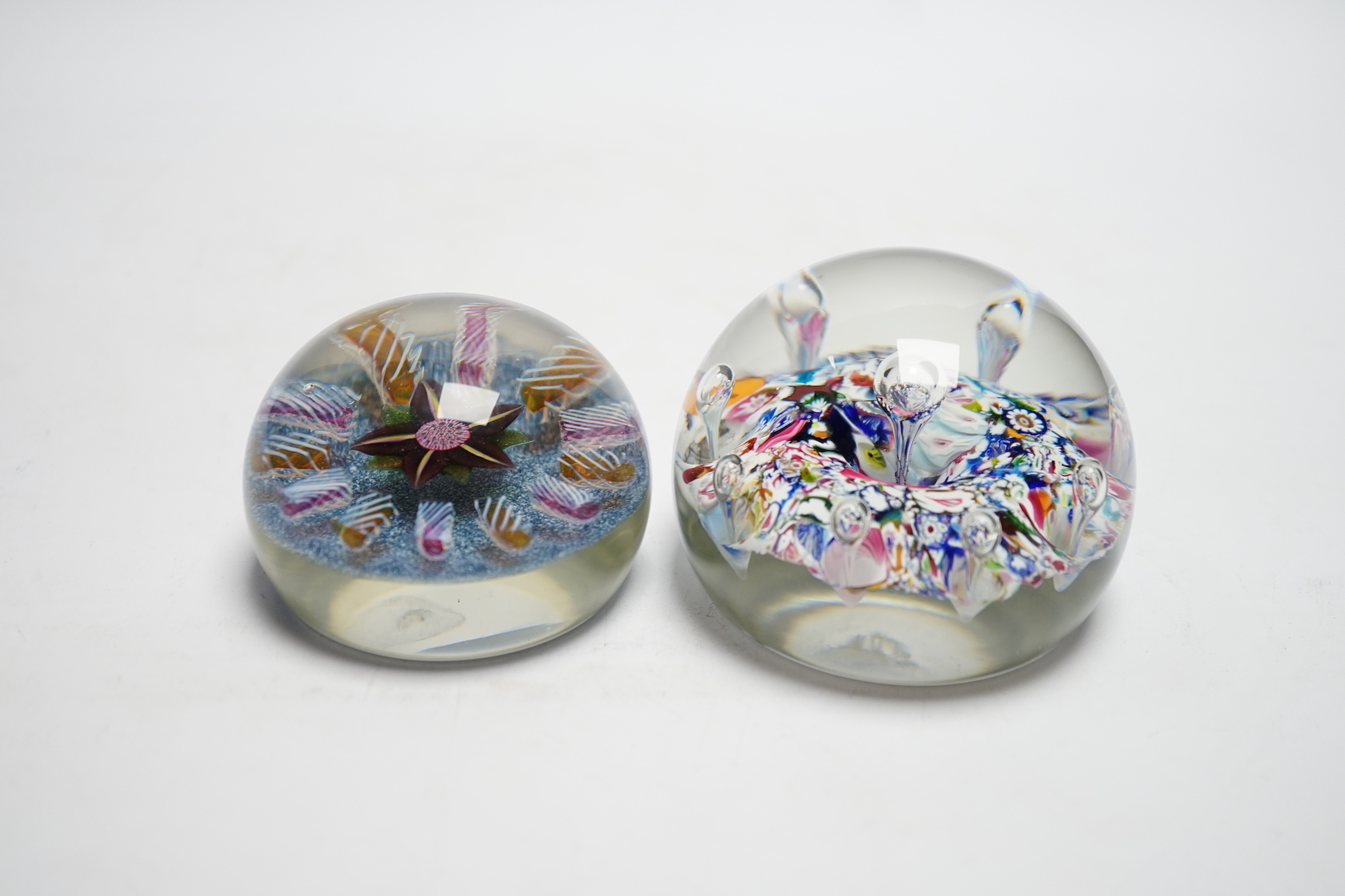 Two Paul Ysart glass paperweights, comprising a purple flower and latticino spoke on a blue jasper ground, ‘H’ cane, PY label, 7cm and ‘Harlequin’ glass paperweight, PY paper label, 8cm